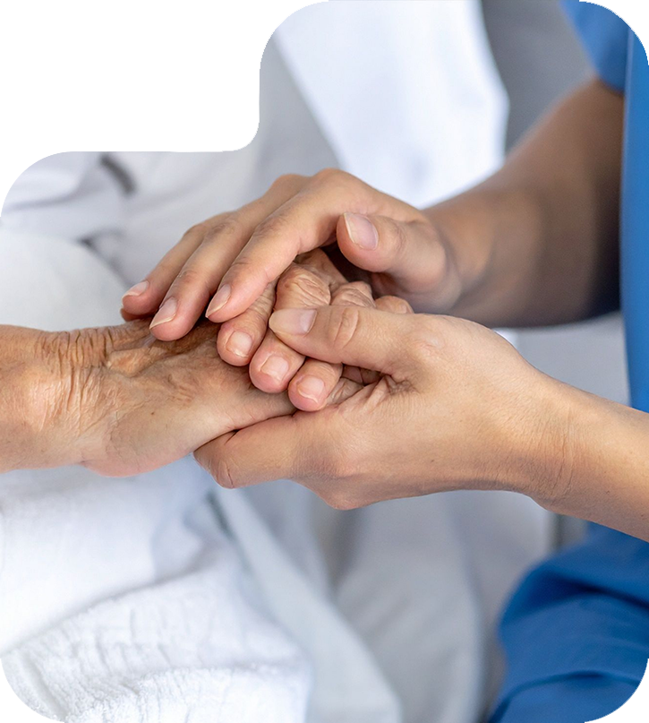 Uśmiechnięta opiekunka zwrócona twarzą do starszej pani siedzącej na wózku inwalidzkim.